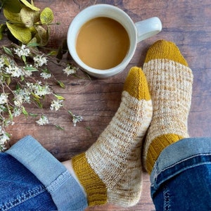 May include: A pair of knitted socks with a yellow and white striped pattern. The socks have a yellow cuff and are worn with blue jeans.