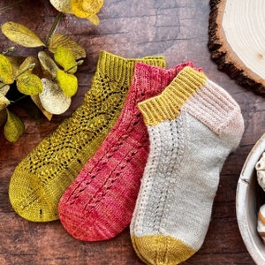 May include: Three pairs of knitted socks in different colors: mustard yellow, red, and cream with a mustard yellow cuff. The socks have a lacy pattern.