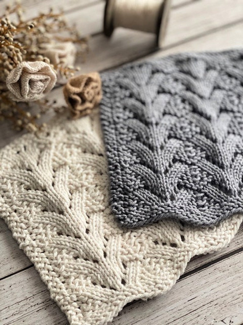 May include: Two knitted dishcloths, one in a light cream color and the other in a dark gray color. Both dishcloths feature a cable knit pattern.