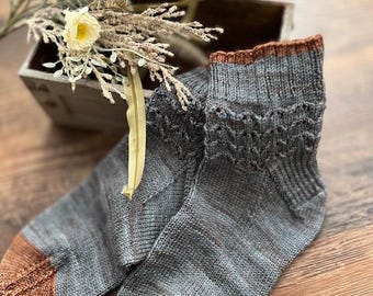 May include: A pair of gray knitted socks with a brown cuff. The socks have a textured pattern and are made of a soft, comfortable material.