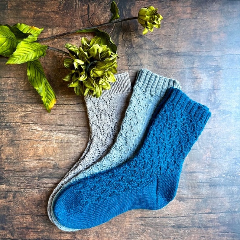May include: Three pairs of knitted socks, one pair is blue, and two pairs are gray. The socks are laid out on a wooden surface.