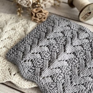 May include: Two knitted dishcloths, one white and one gray, with a delicate lace pattern. The gray dishcloth has a more intricate design.