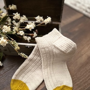 May include: A pair of white knitted socks with yellow heels and toes. The socks are made with a delicate stitch pattern.