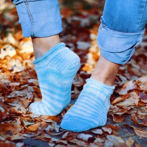 Peut inclure: Une paire de chaussettes de cheville rayées bleu et blanc avec un bord côtelé. Les chaussettes sont portées par une personne debout sur un lit de feuilles mortes.