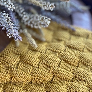 May include: A close-up of a knitted fabric with a textured, waffle-like pattern. The fabric is a deep mustard yellow color.