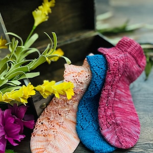 May include: Three pairs of hand-knitted socks in a variety of colors and patterns. The socks are made with a delicate lace stitch and are displayed on a wooden surface.