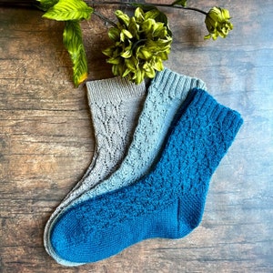 May include: Three pairs of knitted socks in blue and gray. The socks are folded and arranged on a wooden surface.