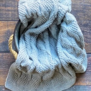 May include: A soft, gray knitted blanket with a cable knit pattern.