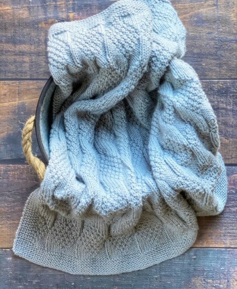 May include: A soft, gray knitted blanket with a cable knit pattern.