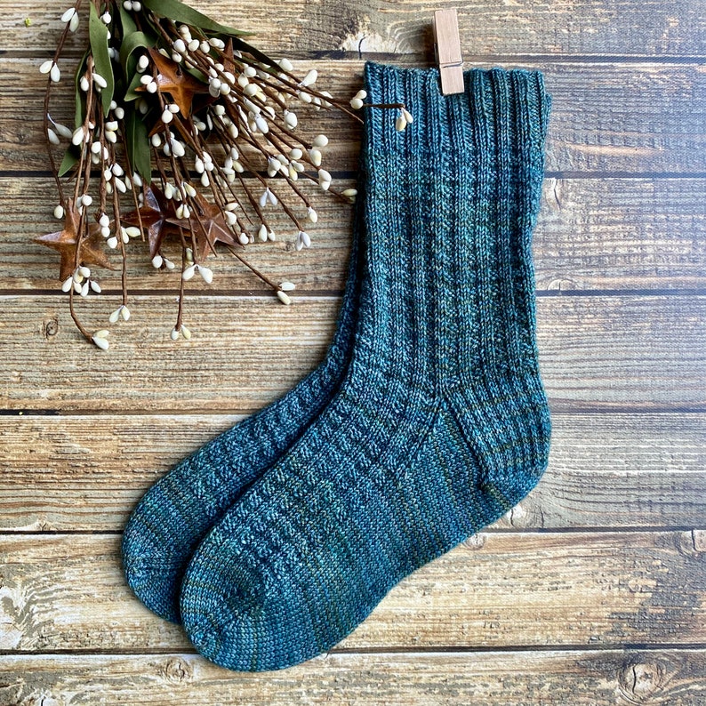 May include: A pair of blue and green knitted socks with a textured pattern. The socks are folded and displayed on a wooden surface.