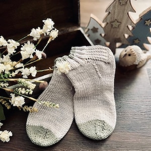 Peut inclure: Une paire de chaussettes en tricot de couleur gris clair avec un orteil et un talon verts. Les chaussettes sont posées sur une surface en bois.