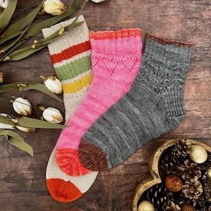 May include: Three pairs of knitted socks in various colours. One pair is beige with red, green, and yellow stripes. Another is pink with a heart pattern. The third pair is grey with a brown cuff and toe.