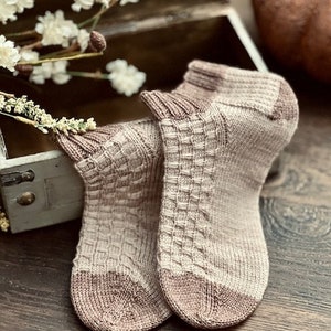 May include: A pair of knitted socks in a beige and light brown colour scheme. The socks have a textured pattern and are folded over at the top.