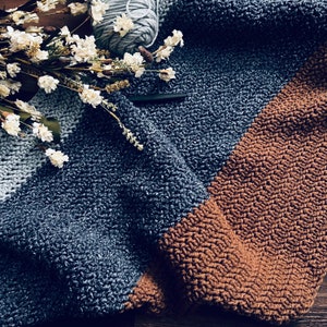 May include: A soft, cosy blanket with a blue and brown colour scheme. The blanket is made of a textured yarn and has a diagonal stripe pattern.