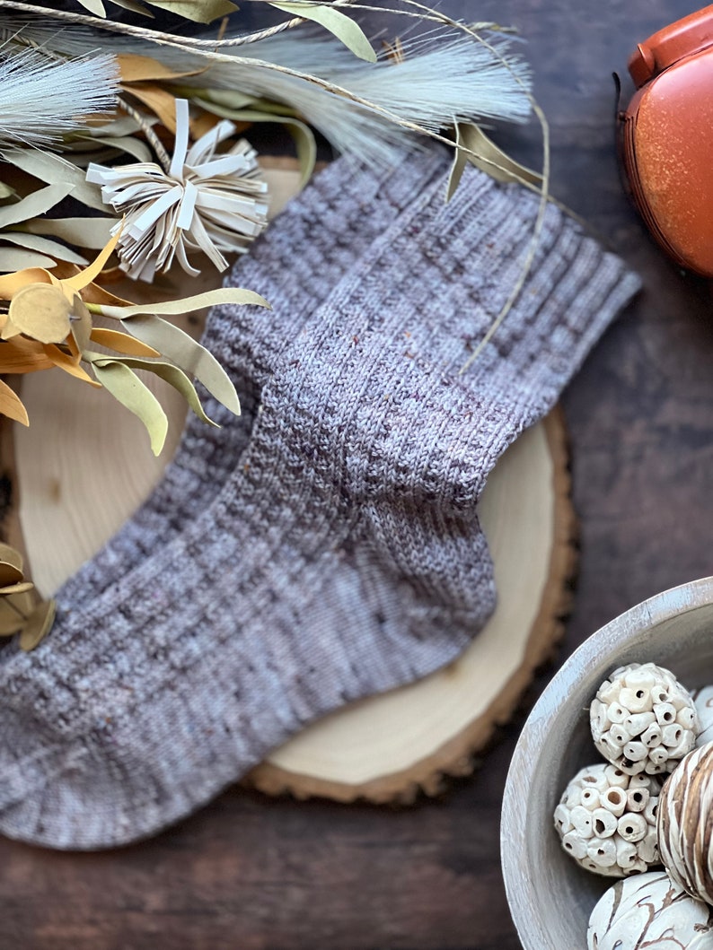 May include: A pair of gray and brown knitted socks with a textured pattern. The socks are lying on a wooden surface.