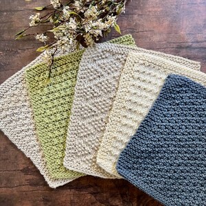 Pu&ograve; includere: Cinque strofinacci a maglia in vari colori e motivi. I panni sono disposti a ventaglio, con il panno verde in basso e il panno grigio in alto. I panni sono realizzati con una maglia testurizzata.