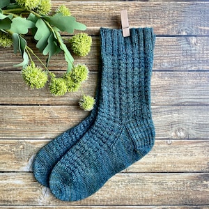 May include: A pair of blue and green knitted socks with a textured pattern. The socks are hanging on a wooden clothes peg.