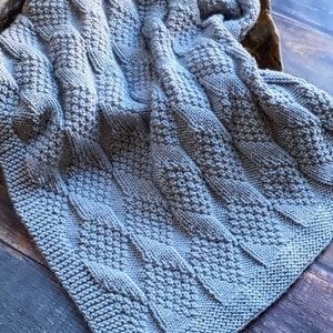 May include: A gray knitted baby blanket with a textured cable knit pattern.