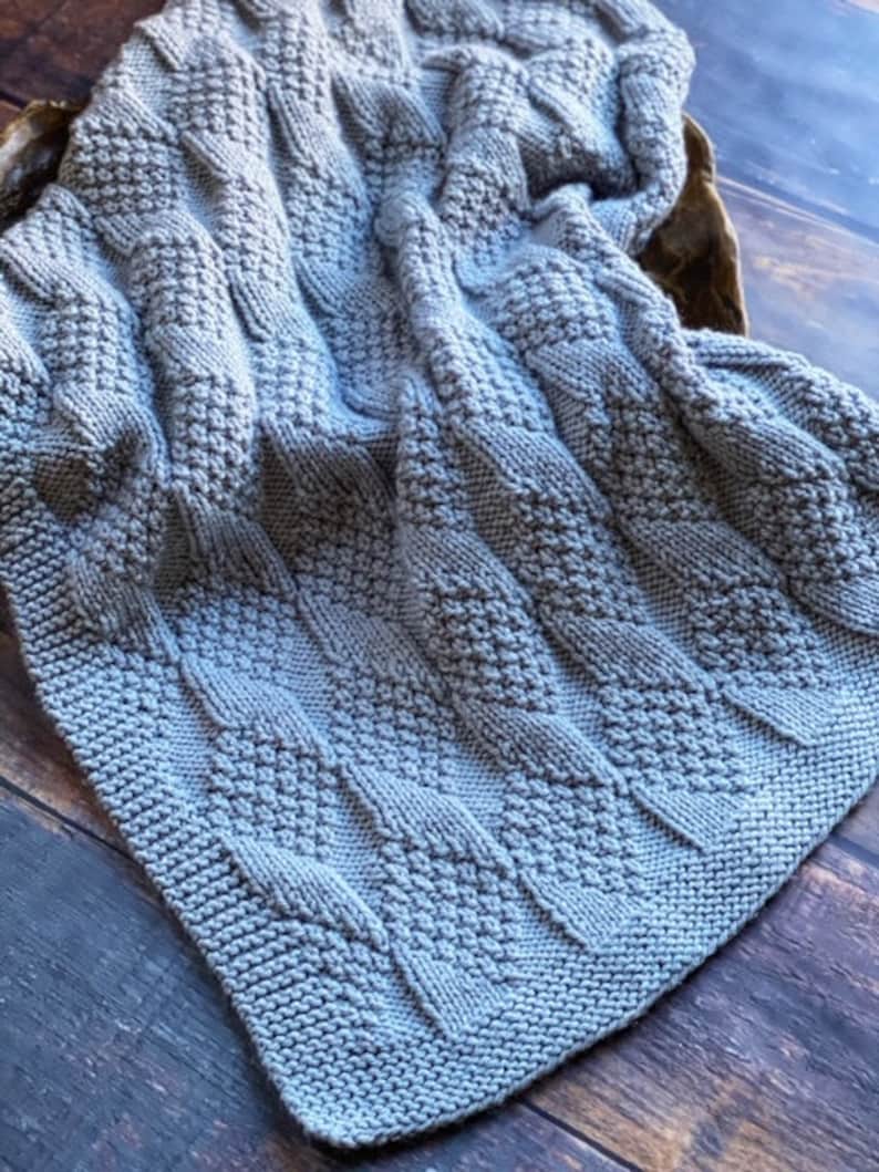 May include: A gray knitted baby blanket with a textured cable knit pattern.