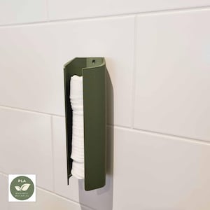 Può includere: Un distributore a parete verde oliva che contiene una pila di asciugamani di carta bianchi. Il distributore è realizzato in un materiale liscio e opaco ed è montato su una parete piastrellata bianca. Il distributore ha un design curvo e un piccolo foro nella parte superiore per il montaggio.