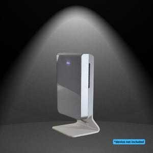 Peut inclure: Un appareil électronique blanc rectangulaire avec un panneau latéral argenté et un petit voyant bleu, monté sur un support blanc assorti. L'appareil présente une surface avant lisse et brillante sur un fond sombre.