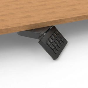 Puede incluir: Vista de cerca de un panel de control negro con múltiples botones, montado debajo de un escritorio de madera. El escritorio tiene un acabado marrón claro. El panel de control es probablemente para ajustar la altura del escritorio.