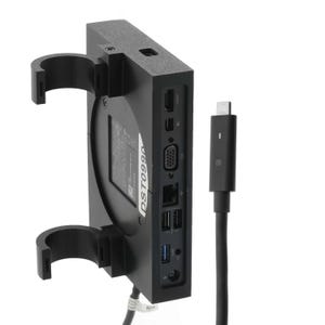 May include: A black computer device with multiple ports, including USB and HDMI, is mounted on a black bracket. A black cable with a USB-C connector is plugged into the device. The device has the text "DST0990" printed on it.