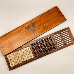 May include: A wooden game box with a dark stain, open to reveal a compartment for pin tokens and dice. The box lid features an engraved emblem. The dice are cream-colored with black text. The words "Pin Tokens", "Vehicle status", and "EMBEREDGE" are visible.