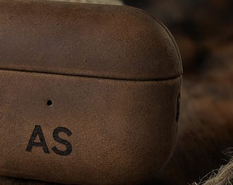 May include: Close-up of a brown leather case with the initials "AS" embossed on the front. The case has a textured surface and a rounded shape, suggesting it's designed to protect small electronics.