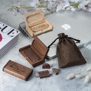 以下が含まれることがあります： 木製のUSBフラッシュドライブとケース。一部にはテキストが刻印されています。ケースの1つは開いており、「Our Wedding」と刻印されたUSBドライブが表示されています。別のケースも開いており、「F & L」と刻印されたUSBドライブが表示されています。小さな茶色の巾着袋も存在します。