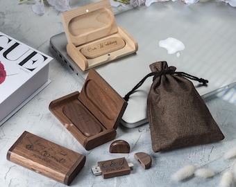 May include: Wooden USB flash drives and cases, some engraved with text. One case is open, displaying a USB drive with "Our Wedding" engraved on it. Another case is open, showing a USB drive with "F & L" engraved. A small brown drawstring bag is also present.