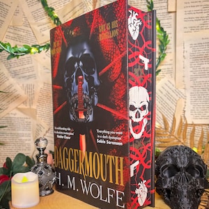 Pode incluir: Um livro de capa dura intitulado DaggerMouth de H. M. Wolfe com uma capa preta e vermelha apresentando um crânio com uma adaga na boca. A lombada exibe um padrão repetitivo de crânios, corações e pistolas brancas sobre um fundo vermelho e preto.
