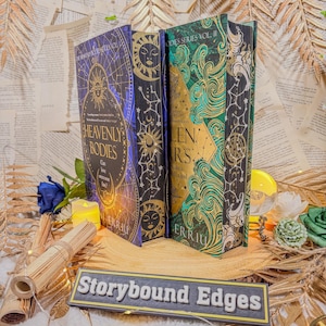 May include: Three hardback books with celestial designs. The spines feature sun and star motifs, with titles like "Heavenly Bodies" and "Stargazers." The books are displayed on a decorative surface with the text "Storybound Edges."
