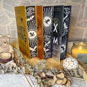 May include: Five fantasy novels with black and gold covers featuring dragon illustrations. The books are titled "Fourth Wing", "Nine", "X", "M", and "The Dragon Guardian".