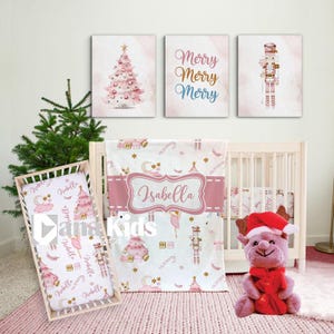 May include: A nursery set with a pink and white Christmas theme. Includes a crib sheet, blanket with the name "Isabella", and wall art with a Christmas tree, nutcracker, and the words "Merry Merry Merry". A plush reindeer toy is also present.