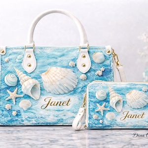 May include: A handbag and matching wallet set with a beach theme. The blue bags feature seashells, starfish, and the name "Janet" in gold script. The bags have white handles and straps.