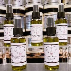 May include: Several bottles of insect and bug repellent are displayed. The bottles are clear with black spray tops and white labels. The labels read "Insect & Bug Repellent" and "DEET Free". The liquid inside is a yellow-green color.