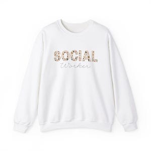 Könnte beinhalten: Weißer Pullover mit einem floralen "SOCIAL WORKER"-Design.