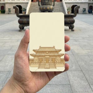 以下が含まれることがあります： ベージュ色の長方形のカード。伝統的なアジアの寺院の詳細なイラストが描かれています。カードは、多層の屋根と複雑な建築的詳細を持つ寺院の前で保持されています。
