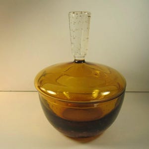 May include: Amber glass sugar bowl with a clear glass lid and handle. The bowl has a textured surface and the lid has a clear glass knob.