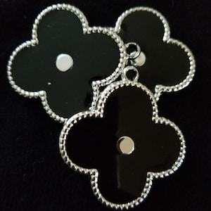 May include: Three black clover-shaped charms with silver beaded edges and a silver circle in the center of each charm.