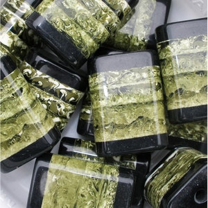 May include: A group of square-shaped, green and black patterned glass beads. The beads have a marbled effect with black lines running through them.