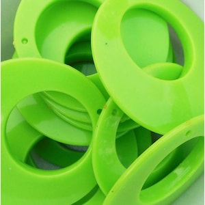 May include: A close-up shot of several bright green, oval-shaped plastic rings. Each ring has a hole drilled near the top. The rings are stacked and overlapping, creating a layered effect. The color is a vibrant, almost neon, green.