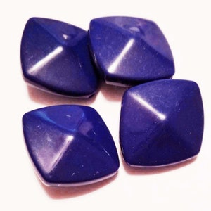 May include: Four dark blue square-shaped beads with a pyramid-shaped top. The beads are made of a smooth, glossy material.