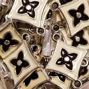 May include: Close-up of a silver chain with multiple cream-colored links, each featuring a black four-leaf clover design.