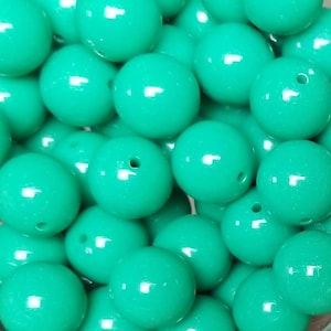 May include: A collection of round, smooth, solid turquoise beads with a glossy finish. Each bead features a single centered hole for threading. The beads are clustered together, displaying a uniform bright color and a reflective surface texture.
