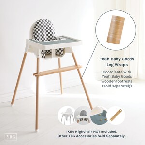 May include: A white highchair with wooden legs and a checkered seat and backrest. The highchair has a gray tray and a wooden footrest. The image also shows leg wraps and mentions coordinating wooden footrests.
