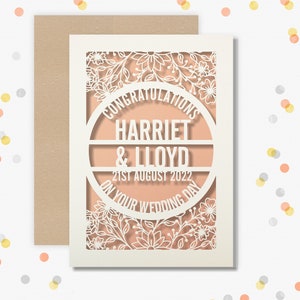 May include: White wedding card with a cut-out design featuring a floral pattern and the text "Congratulations Harriet & Lloyd 21st August 2022 On Your Wedding Day".