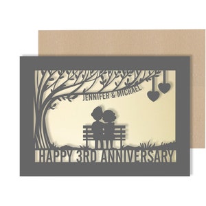 May include: A grey card with a laser cut design of a couple sitting on a bench under a tree. The text "Jennifer & Michael" and "Happy 3rd Anniversary" is included.