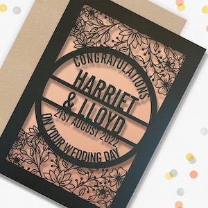 May include: A black and white laser cut wedding card with a floral design. The card says "Congratulations Harriet & Lloyd on your wedding day 21st August 2022".